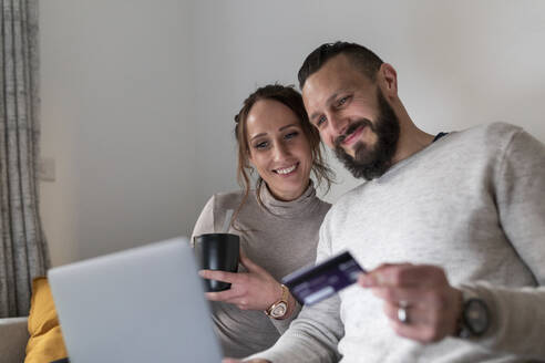 Lächelndes Paar beim Online-Shopping mit dem Laptop zu Hause - WPEF03720