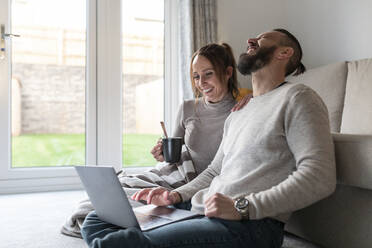 Mann lacht, während er mit seiner Freundin zu Hause einen Film auf dem Laptop anschaut - WPEF03721