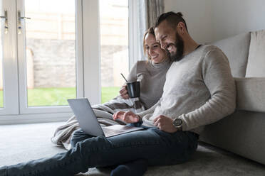 Glückliches Paar sieht sich im Wohnzimmer zu Hause einen Film auf dem Laptop an - WPEF03722