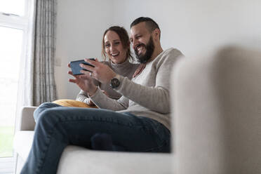Glückliches Paar, das ein Smartphone benutzt, während es zu Hause sitzt - WPEF03729