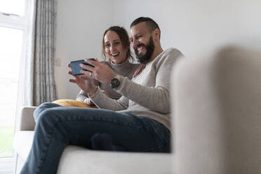 Happy couple using smart phone while sitting at home - WPEF03729