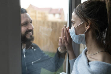 Paar, das sich während des Ausbruchs von COVID-19 am Fensterglas berührt - WPEF03734