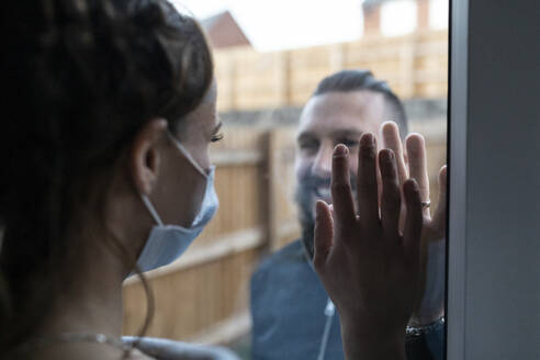 Couple touching hands from window glass during COVID-19 pandemic - WPEF03736
