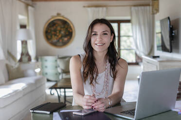 Smiling female event planner sitting by laptop at home - EIF00323