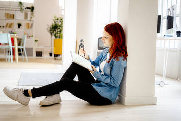 Junge Geschäftsfrau arbeitet an einem digitalen Tablet, während sie sich im Büro auf eine Säule stützt - GIOF09856