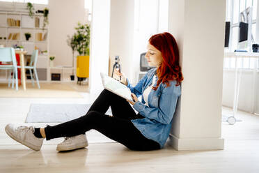 Young businesswoman working on digital tablet while leaning on pillar at office - GIOF09856