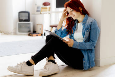 Smiling woman with head in hands using digital tablet while sitting on floor at office - GIOF09859