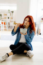 Young businesswoman eating noodles while sitting on floor at office - GIOF09863