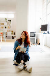 Businesswoman eating noodles while sitting on floor at office - GIOF09864