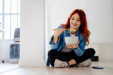 Businesswoman smiling while eating noodles at office - GIOF09869