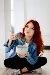 Smiling businesswoman eating noodles while sitting at office - GIOF09870