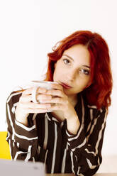 Geschäftsfrau hält Kaffeetasse, während sie im Büro sitzt - GIOF09909