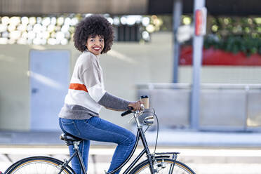 Happy woman looking away while sitting on bicycle at railroad station - GGGF00236