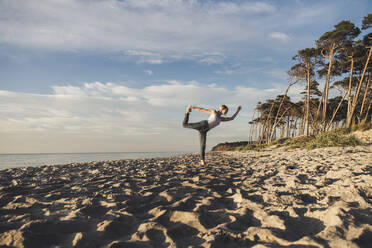 Active woman practicing yoga at beach against sky on sunny day - CHPF00712