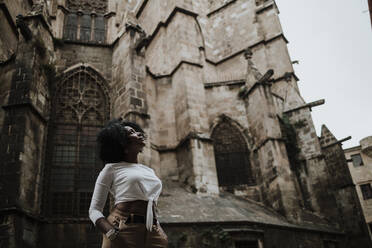 Nachdenkliche Frau, die nach oben schaut, während sie vor der Kathedrale von Barcelona steht, Barcelona, Spanien - GMLF00853