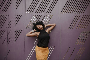 Carefree woman with hand in hair leaning on metal wall - GMLF00867