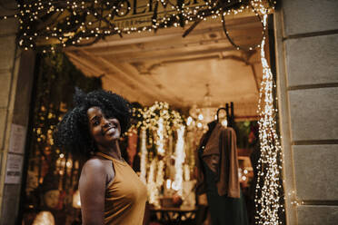 Lächelnde Frau vor einem beleuchteten Geschäft bei Nacht - GMLF00874