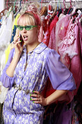 Auffällige Geschäftsfrau mit Hand an der Hüfte, die in ihr Smartphone spricht, vor einem Kleiderständer - FLLF00527
