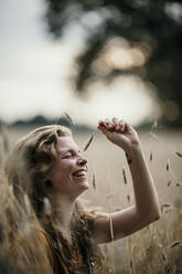 Frau lächelnd beim Spielen mit der Ernte auf einem landwirtschaftlichen Feld - MJRF00280