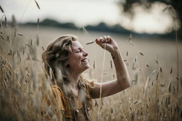 Glückliche Frau sitzt mit geschlossenen Augen in einem landwirtschaftlichen Feld - MJRF00281