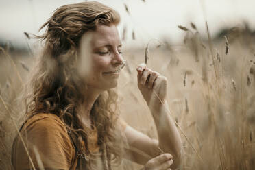 Frau riecht an der Ernte, während sie auf einem landwirtschaftlichen Feld sitzt - MJRF00282