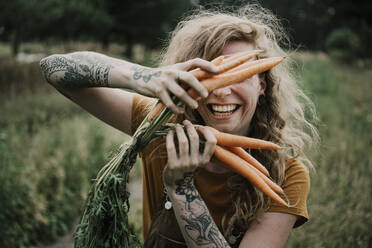Bäuerin lächelt und hält Karotten auf dem Bauernhof - MJRF00299