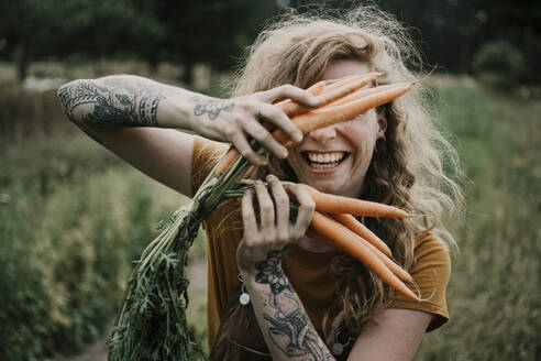 Female farmer smiling while holding carrots at farm - MJRF00299