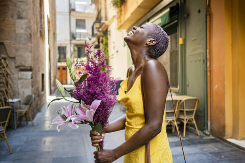 Cheerful woman with flowers standing by sidewalk cafe in city - RCPF00446