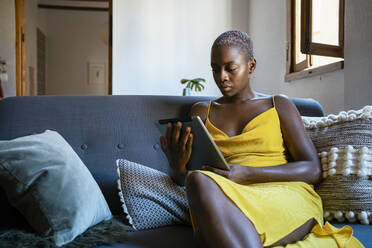 Frau benutzt digitales Tablet, während sie zu Hause auf dem Sofa sitzt - RCPF00454