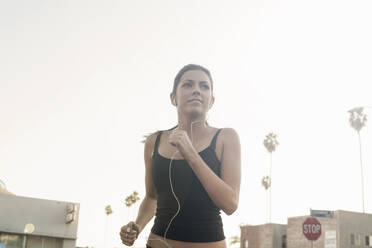 Confident woman jogging while listening music against clear sky - AJOF00722