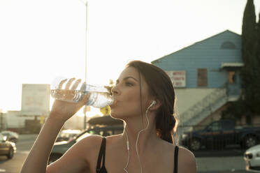 Junge Frau trinkt Wasser aus einer Flasche in der Stadt bei Sonnenuntergang - AJOF00726