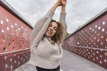 Lächelnde Frau, die auf einer Brücke stehend ihre Hand gegen den Himmel streckt - MEF00016