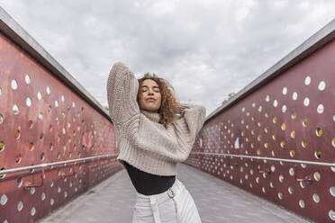 Young woman with hands behind head dancing on bridge against sky - MEF00017