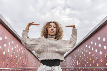 Young woman wearing sweater dancing while standing against sky - MEF00018