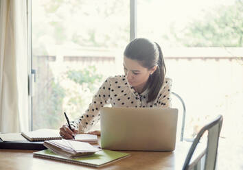 Businesswoman using laptop while writing in book at office - AJOF00739