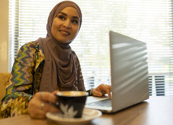 Junge Frau mit Laptop, die in einem Café sitzt und wegschaut - JCCMF00044