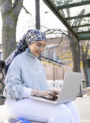 Junge Frau lächelt bei der Arbeit am Laptop im Freien - JCCMF00058