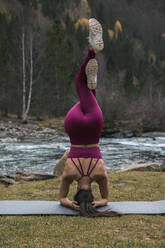 Active young woman practicing headstand pose with intertwined legs on yoga mat at Ordesa National Park, Huesca, Spain - ACPF00938