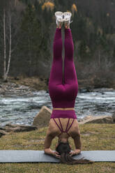 Active young woman practicing headstand pose on yoga mat at Ordesa National Park, Huesca, Spain - ACPF00941