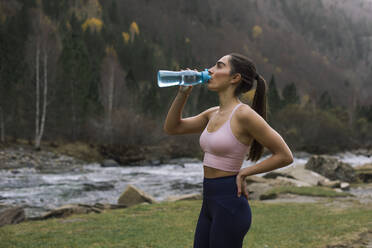 Erschöpfte junge Frau, die Wasser trinkt, während sie mit der Hand auf der Hüfte steht, Ordesa-Nationalpark, Huesca, Spanien - ACPF00943