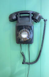 Vintage rotary landline phone hanging on turquoise wooden wall at barber shop - AJOF00753