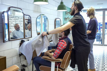 Männlicher Friseur mit Schürze vor einem Kunden im Friseursalon - AJOF00758