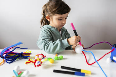 Nettes Mädchen macht kreatives Spielzeug aus Pfeifenreinigern und Styroporkugel am Tisch - GEMF04421