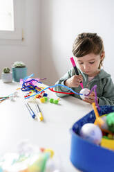 Mädchen lernt, kreatives Spielzeug aus Pfeifenreinigern und Styroporkugeln am Tisch an der Wand herzustellen - GEMF04422