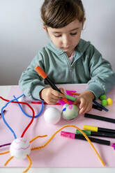 Mädchen färbt Styroporkugel mit Skizzenstift auf Tisch - GEMF04428