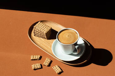 Keramik-Tasse mit leckerem Kaffee in der Nähe von knusprigen Crackern auf einem Holzteller in einem Café im Sonnenlicht von oben - ADSF18415