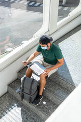 Ein männlicher Tourist sitzt auf einer Treppe im Flughafen und surft auf seinem Netbook, während er auf den Abflug wartet (von oben) - ADSF18423