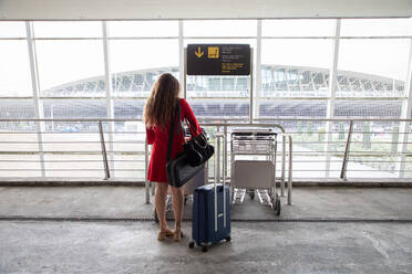 Back view of traveling female in airport collecting a baggage trolley and waiting for flight - ADSF18424