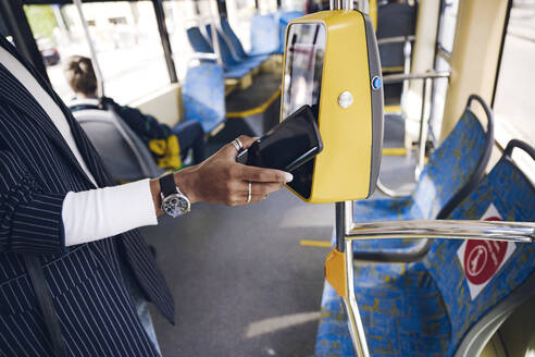 Junge Frau, die mit ihrem Smartphone eine Busfahrkarte bezahlt - VYF00284