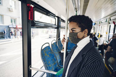 Young businesswoman looking through window while traveling in bus during COVID-19 - VYF00304